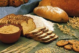 Assorted gluten-containing foods including sliced bread, flour, wheat grains, and cookies.