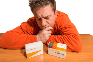 Man in orange sweater comparing boxes of paracetamol and ibuprofen tablets on table