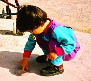 Young child in colorful clothing crouching and touching the ground outdoors