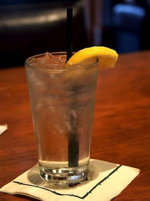 Glass of iced diet soda with lemon wedge and a straw on a napkin, wooden table background
