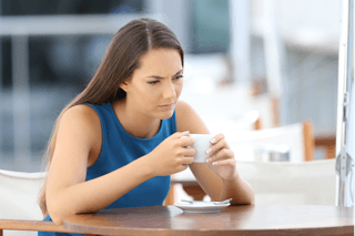 Young woman in blue dress looking thoughtful while holding a coffee cup outdoors