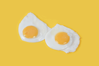 Two sunny side up eggs on a yellow background, illustrating dietary cholesterol