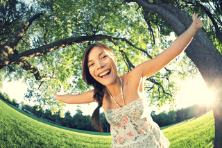 Young woman smiling with arms outstretched outdoors in bright green park sunlight