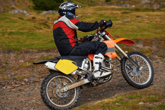 Motocross rider in protective gear riding dirt bike on rocky outdoor trail