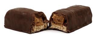 Close-up of a chocolate-covered candy bar split in half, showing caramel and nougat layers