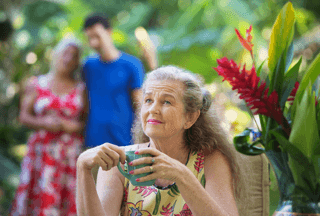 Older woman enjoying coffee in lush garden, family in background, healthy lifestyle theme