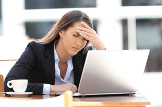 Stressed woman at laptop, hand on forehead, feeling overwhelmed while working at a desk