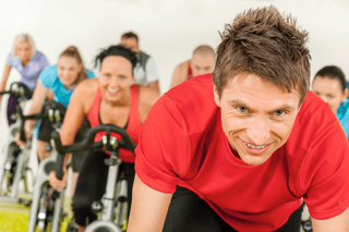 Group indoor cycling class with smiling people, exercise bikes, and energetic atmosphere