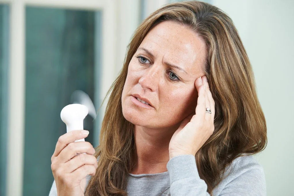 Woman holding scalp massager, touching temple, showing health concern indoors