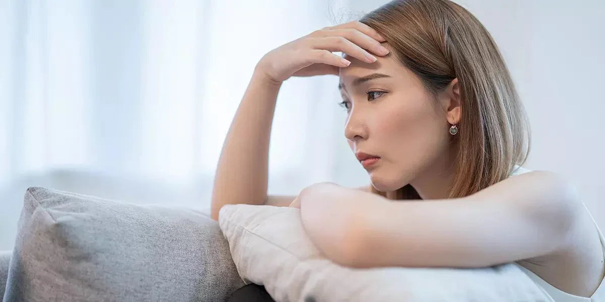 Thoughtful woman sitting on couch, resting head on arm, looking pensive indoors