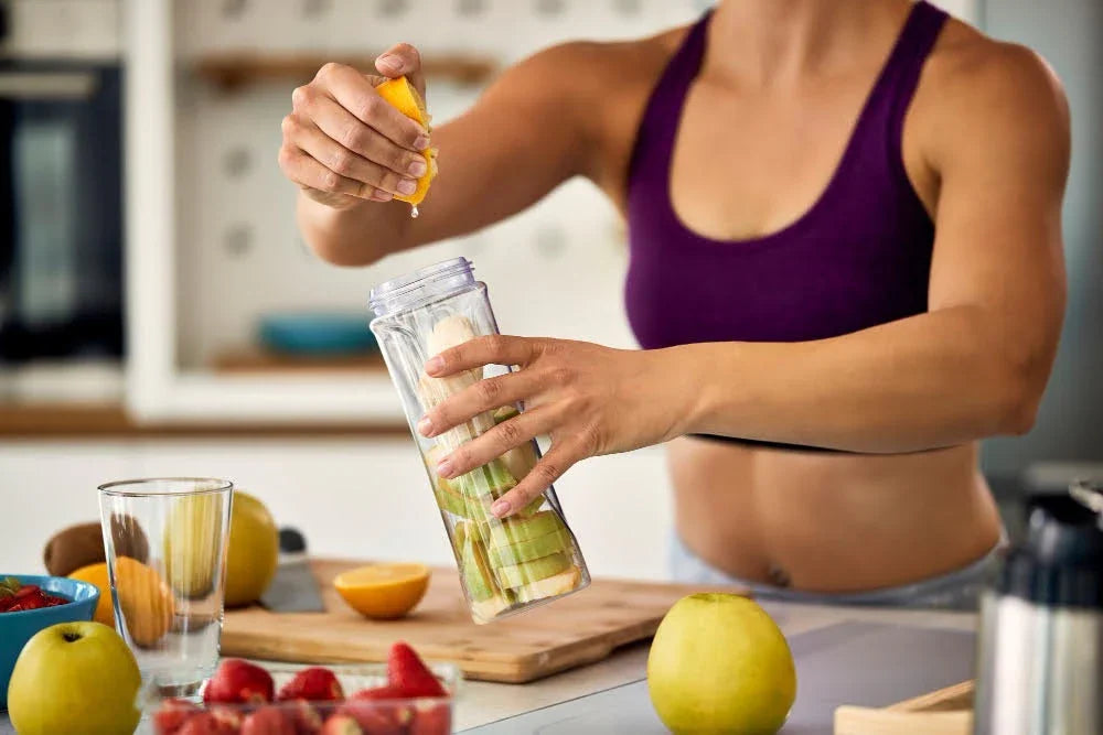 Woman in athletic wear preparing a healthy fruit smoothie with fresh apples and strawberries